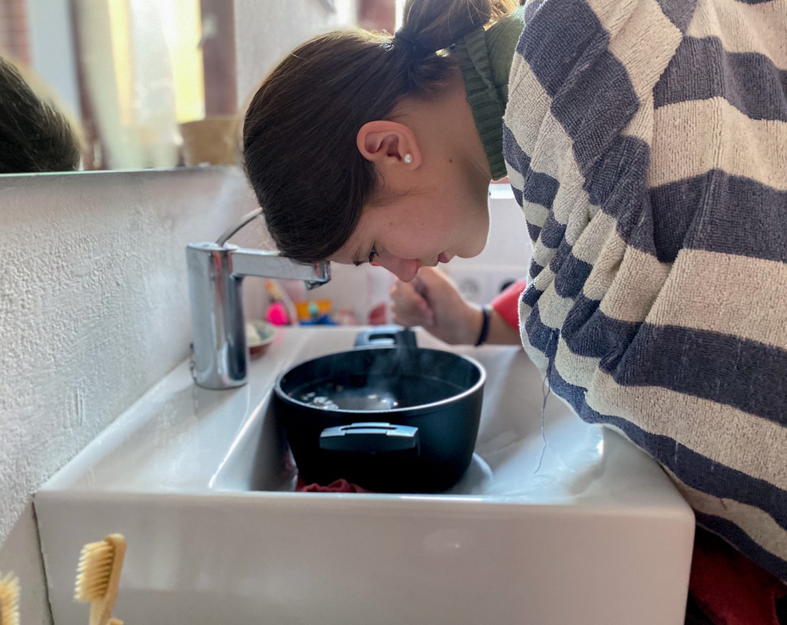 Woman breathing in steam from a large bowl of water.
