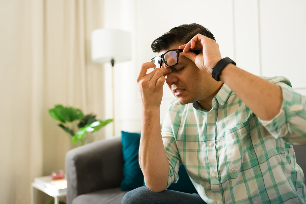 Man lifting his glasses to hold his sore sinuses.